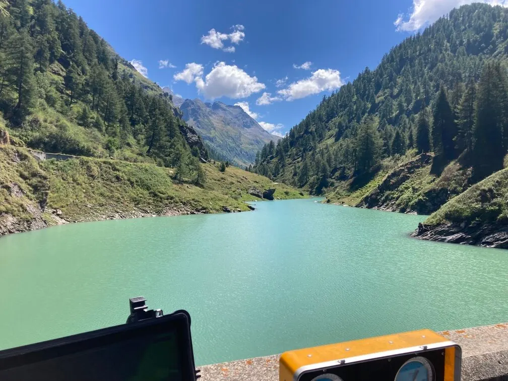 Specchio d'acqua turchese di un bacino idroelettrico tra le montagne, visto dal mezzo di lavoro