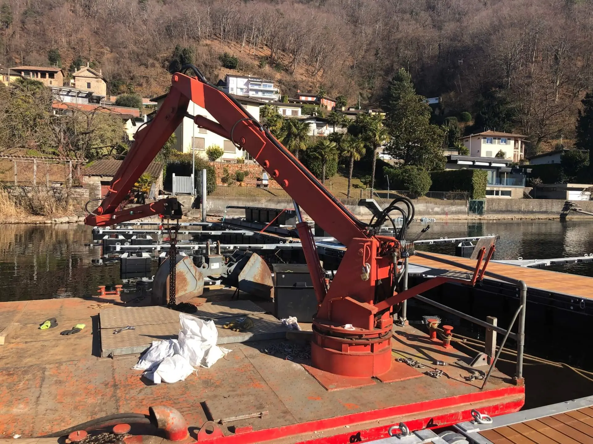 Pontone con gru rossa ormeggiato accanto a un pontile galleggiante in costruzione, sul lago