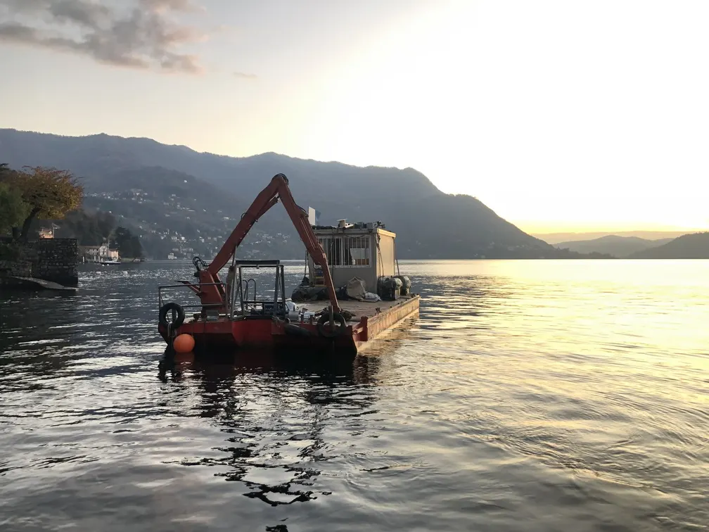 Zattera con escavatore sul lago di Como al tramonto